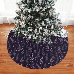 May include: A dark purple Christmas tree skirt with a botanical pattern featuring ferns, mushrooms, moons, and berries. The skirt is circular and sits beneath a decorated Christmas tree.