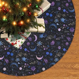 May include: A black Christmas tree skirt with a celestial floral design. The skirt features crescent moons, stars, and various flowers in shades of blue, purple, and gray. A decorated Christmas tree and wrapped gifts are partially visible.