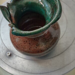 Könnte beinhalten: Eine braune Keramikvase mit grüner Glasur. Die Vase hat eine einzigartige, unregelmäßige Form mit einer breiten Öffnung oben.