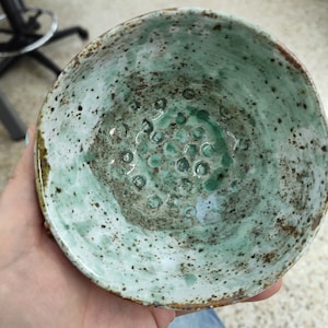 May include: A green ceramic bowl with a speckled glaze and a pattern of small circles in the center.
