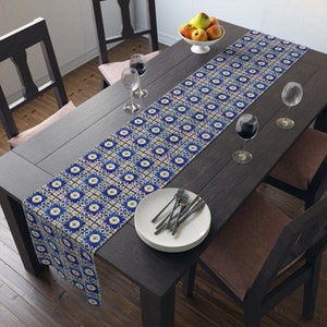 May include: A blue and white patterned table runner with a geometric design. The runner is placed on a dark wood table with two chairs and a bowl of fruit.