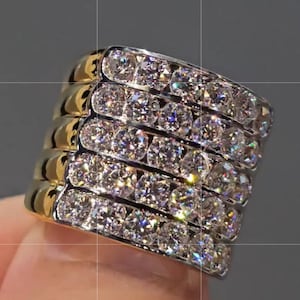 May include: A gold and diamond ring with five bands. Each band is set with multiple round-cut diamonds. The ring has a gold band on the top and bottom of each diamond band. The ring is held by a person's finger.