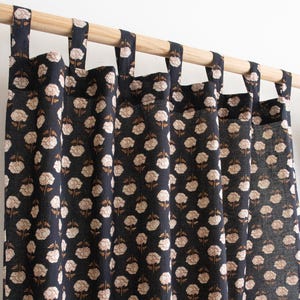 May include: Navy blue curtains featuring a repeating floral pattern in cream and brown. The curtains are suspended from a wooden pole with fabric loops. The floral design adds a touch of elegance to the room.