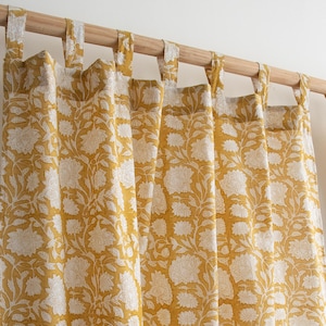 Könnte beinhalten: Senfgelbe Vorhänge mit weißem Blumenmuster. Die Vorhänge hängen an einer Holzstange mit Stoffschlaufen. Das florale Design ist ein sich wiederholendes Muster aus stilisierten Blumen und Blättern.
