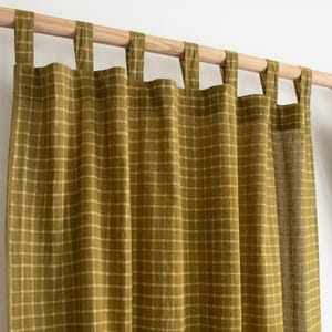 May include: Olive green and beige plaid curtain panels hanging from a wooden rod. The curtains are made of a textured fabric and feature a grid pattern. The tabs at the top allow for easy hanging. The overall aesthetic is simple and natural.