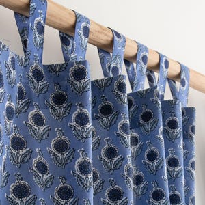 Könnte beinhalten: Blau gemusterte Vorhänge mit Blumenmuster, die an einer Holzstange hängen. Die Vorhänge zeigen ein sich wiederholendes Muster stilisierter Blumen in Blau- und Weißtönen. Die Vorhänge sind aus leichtem Stoff gefertigt und haben Stoffschlaufen zum Aufhängen.