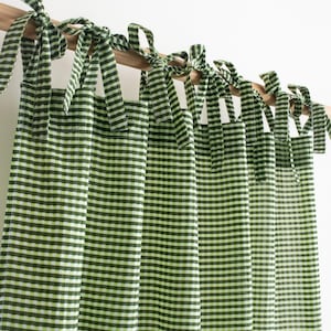 Op de afbeelding: Groen-witte geruite gordijnen met bijpassende striksluitingen. De gordijnen hangen aan een houten roede en de strikken zijn in strikken geknoopt. De stof heeft een klassiek ruitpatroon.