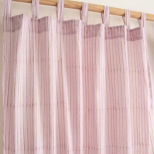 May include: Pink and gold striped curtain panels hanging from a wooden rod. The curtains have vertical stripes in varying shades of pink and gold. The top of the curtains have fabric loops for hanging. The curtains are made of a lightweight fabric.