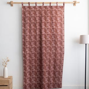 Puede incluir: Una cortina rosa polvoriento con un patr&oacute;n repetitivo de formas org&aacute;nicas marr&oacute;n oscuro. La cortina cuelga de una barra de madera natural con soportes de madera a juego. La cortina est&aacute; hecha de una tela texturizada.