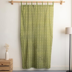 May include: Green curtain with a repeating leaf pattern, hanging from a wooden rod. The curtain is a light green color with darker green leaf designs. The curtain is hanging in front of a white wall.