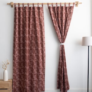 Puede incluir: Dos cortinas a juego, de cuerpo entero, con un estampado floral en tonos marrones y malvas, colgadas de una barra de madera. Una cortina est&aacute; atada con una cinta blanca. Un jarr&oacute;n blanco con flores secas descansa sobre una caja de madera.