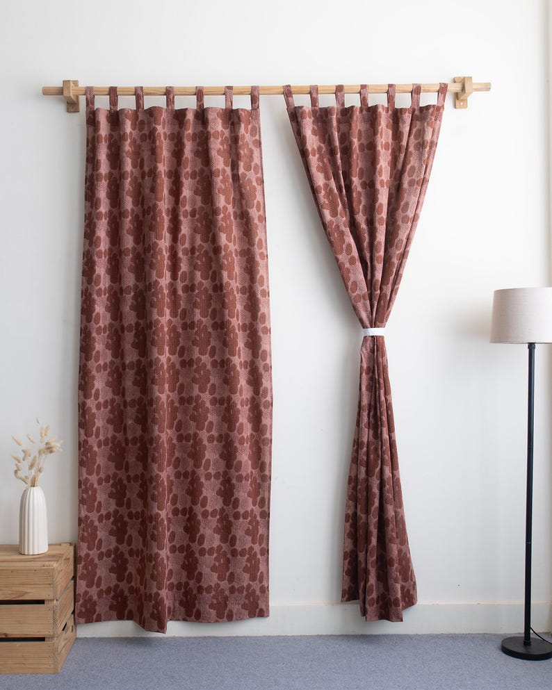 Puede incluir: Dos cortinas a juego, de cuerpo entero, con un estampado floral en tonos marrones y malvas, colgadas de una barra de madera. Una cortina est&aacute; atada con una cinta blanca. Un jarr&oacute;n blanco con flores secas descansa sobre una caja de madera.