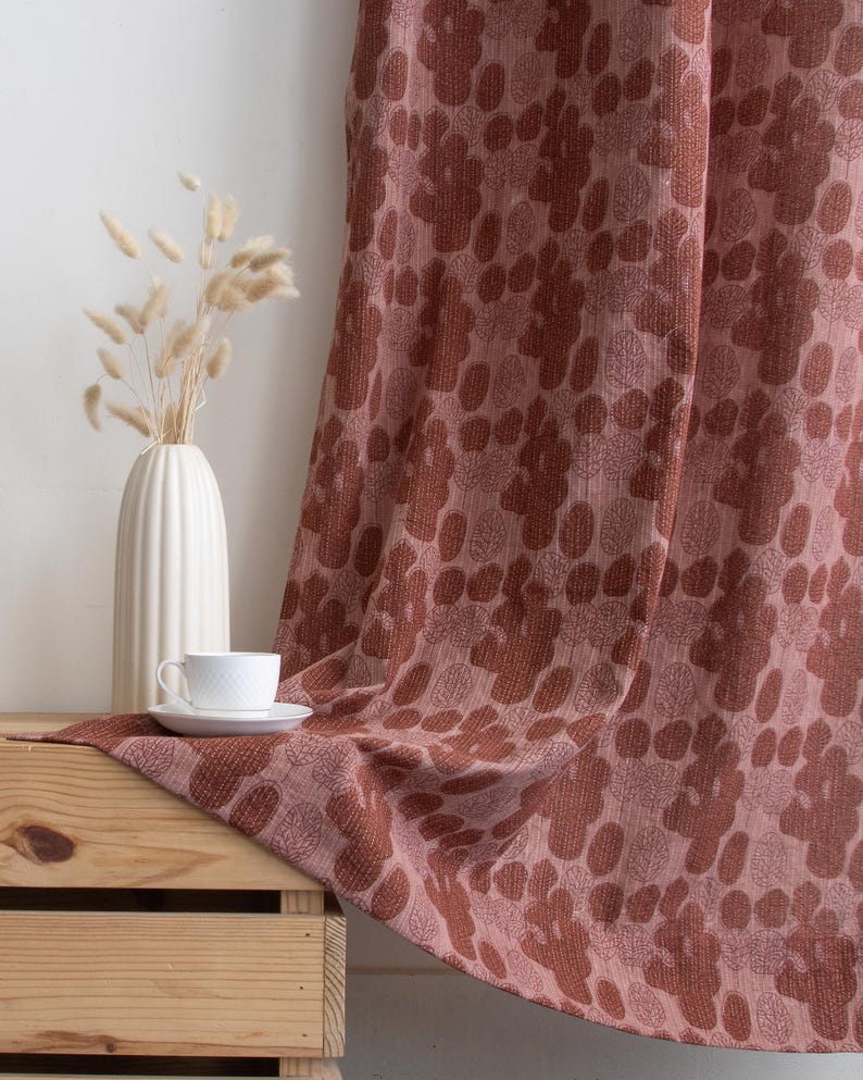 Puede incluir: Una cortina drapeada con un estampado floral en tonos rosa empolvado y marr&oacute;n es el foco principal. Un motivo floral se repite en la tela. Una taza y un platillo blancos descansan sobre una caja de madera, junto a un jarr&oacute;n blanco con flores secas. La escena evoca calidez.