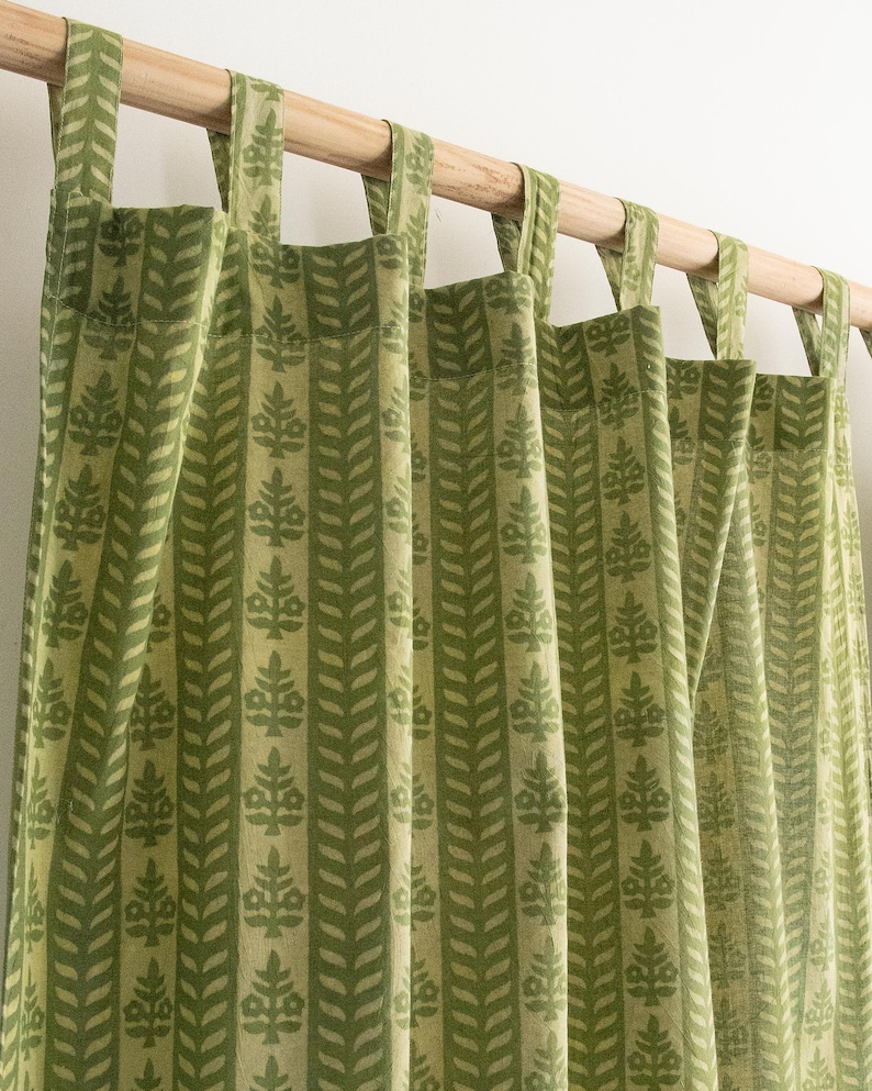 May include: Green and cream-colored curtains with a repeating leaf pattern. The curtains are hanging from a wooden rod with fabric loops. The fabric has a textured appearance, and the design is vertical.