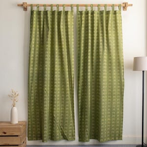 May include: Two green curtains with a repeating leaf pattern hang from a wooden rod. The curtains are a light green color with a darker green leaf design. The curtains are hanging in front of a white wall.