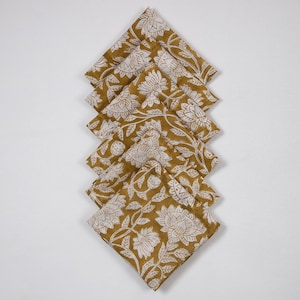 May include: A stack of eight mustard yellow cotton napkins with a white floral pattern. The napkins are folded in a triangular shape.