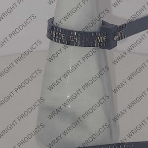 May include: A black cable tie with a white alphabet letter identifier. The letters are A through Z. The cable tie is wrapped around a clear glass bottle.