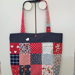 Peut inclure: Un sac fourre-tout patchwork avec une base et des anses en jean. Le sac présente des carrés de tissu avec des motifs de cœurs, de fleurs et de fraises. Les anses sont rouges à pois blancs.