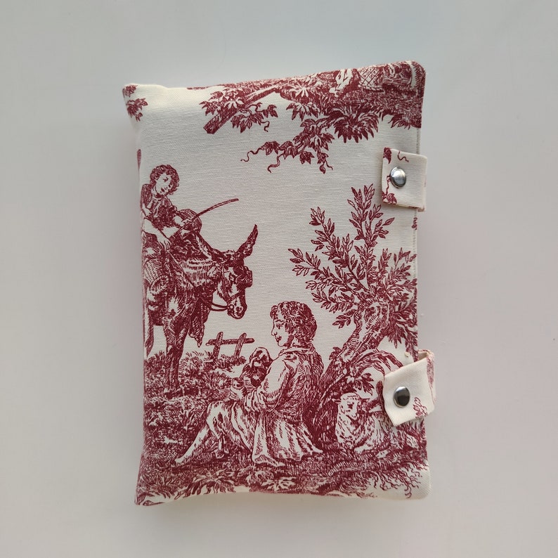 May include: A white fabric pouch with a red toile pattern featuring a shepherdess, a donkey, and a tree. The pouch has two silver snap closures.