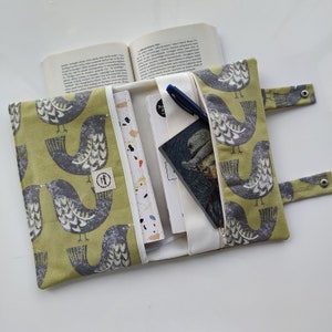 K&ouml;nnte beinhalten: Eine gr&uuml;ne Stofftasche f&uuml;r B&uuml;cher mit einem Vogelmuster. Die Tasche hat einen Rei&szlig;verschluss und ist ge&ouml;ffnet, um ein Buch und ein Notizbuch im Inneren zu zeigen.