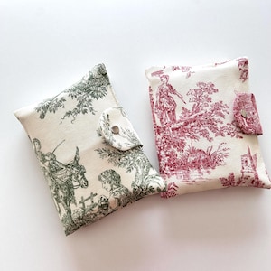 Puede incluir: Dos estuches rectangulares de tela con cierres de broche. Uno presenta un estampado toile de jouy verde oscuro de una persona y un burro sobre fondo crema. El otro presenta un estampado toile de jouy rojo con figuras y árboles.