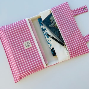 Puede incluir: Una bolsa de cremallera de tela de cuadros rosa y blanco con forro blanco. La bolsa está abierta y contiene un cuaderno, un bolígrafo y un libro. La bolsa tiene una pequeña etiqueta con el texto "Sweet" en ella.