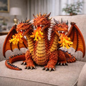 Peut inclure: Sculpture artisanale d'un dragon à trois têtes, aux tons orange et jaune, avec des ailes et des griffes détaillées. Chaque tête crache une flamme de fil jaune et orange. Le dragon est crocheté et posé sur une surface grise.