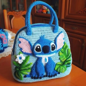 May include: A light blue crochet handbag featuring a blue cartoon character with large ears and a friendly expression. The bag has a matching blue handle and zipper, with pink and green accents. The bag is handmade.