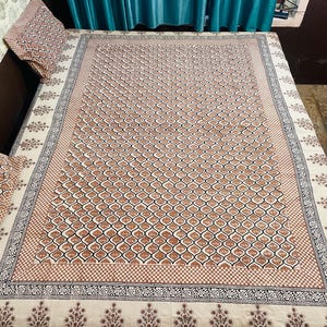 May include: A white cotton bedspread with a brown and black geometric pattern. The bedspread has a decorative border with a floral design.
