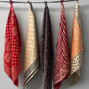 Może przedstawiać: Pięć różnych wzorzystych kwadratów tkaniny wiszących na sznurze do suszenia. Kwadraty są w odcieniach czerwieni, pomarańczy, brązu i kremowego.