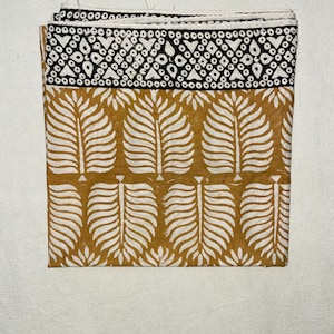 May include: A brown fabric square with a white and black geometric pattern on the top border and a white leaf pattern on the rest of the fabric.