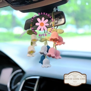 May include: A handmade car charm featuring a cluster of crocheted lily of the valley flowers in various pastel colors, hanging from a rearview mirror. The charm is decorated with a pink daisy and the text "100% Handmade with Love".