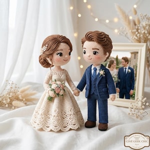 Può includere: Bambole di sposi all'uncinetto che si tengono per mano, con la sposa in un abito color crema e lo sposo in un abito blu. La sposa tiene in mano un bouquet di fiori. Sullo sfondo c'è una foto incorniciata di una coppia. Le bambole sono su una superficie bianca.