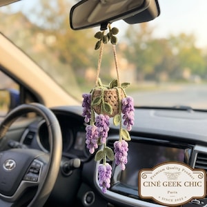 Könnte beinhalten: Gehäkelter Autoanhänger mit einem hängenden Korb mit lila Blauregenblüten und grünen Blättern. Der Anhänger hängt am Rückspiegel. Der Anhänger hat den Text "CINÉ GEEK CHIC PARIS SINCE 2022".
