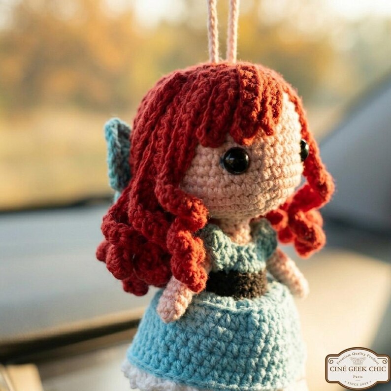 A crocheted doll with red hair and a blue dress is hanging on a string.