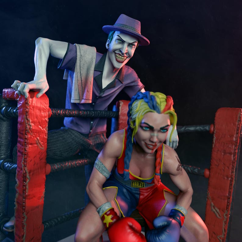 May include: A detailed statue of The Joker and Harley Quinn in a boxing ring. The Joker wears a purple suit and fedora, smiling menacingly. Harley Quinn is in boxing attire, with red and blue gloves, and her signature hair colours.