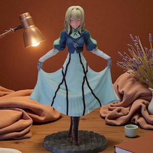 May include: A figurine of a character in a light blue dress with black accents, a blue jacket, and blonde hair. The figure is standing on a gray circular base. The background includes a lamp, books, and a vase with lavender.