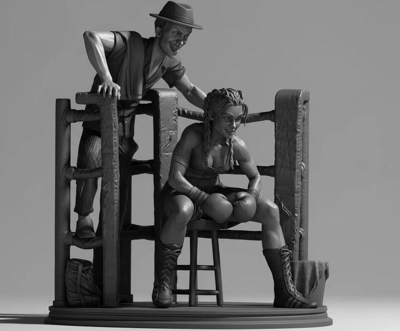May include: A monochrome sculpture depicting a boxing scene. A boxer sits in a ring corner, wearing gloves and boots. A man in a hat leans over the ring, seemingly offering advice. A bag and bucket are also present in the scene.
