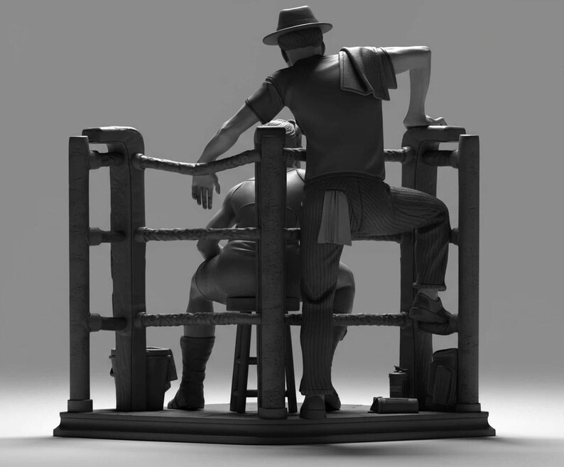 May include: A monochrome sculpture depicting a boxing ring. One figure, wearing a hat and striped trousers, leans on the ropes. Another figure sits on a stool within the ring.