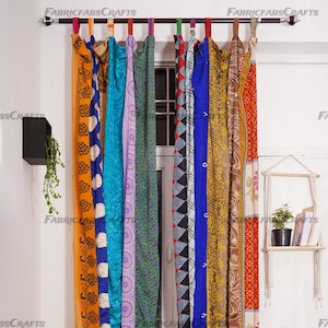 May include: A set of colorful fabric curtains hanging on a white wall. The curtains are made of different fabrics with various patterns and colors, including orange, blue, purple, green, and brown. The curtains are hung on a metal rod with rings.