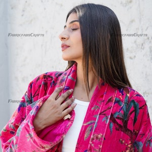 May include: A pink velvet robe with a floral print featuring birds and leaves. The robe has a long sleeve and a sash tie.