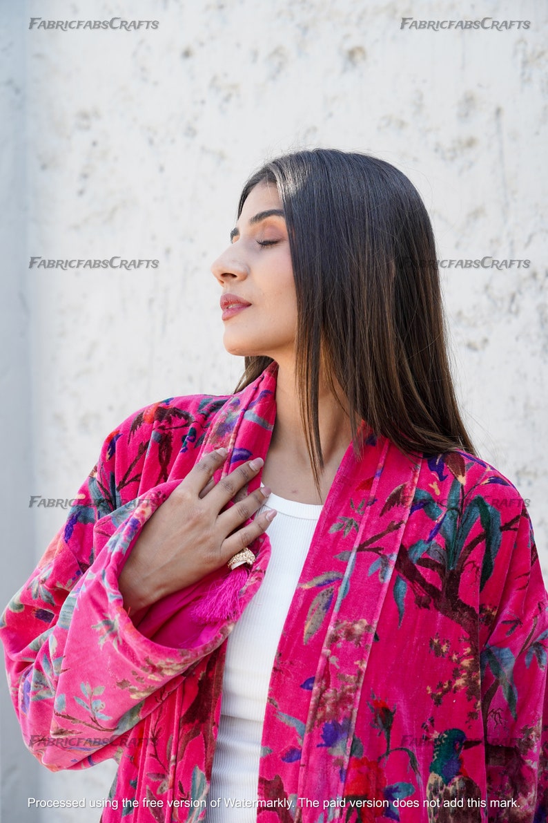 May include: A pink velvet robe with a floral print featuring birds and leaves. The robe has a long sleeve and a sash tie.