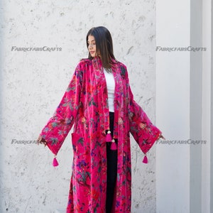 May include: A long, pink velvet robe with a floral print and tassels. The robe has a shawl collar and long sleeves.