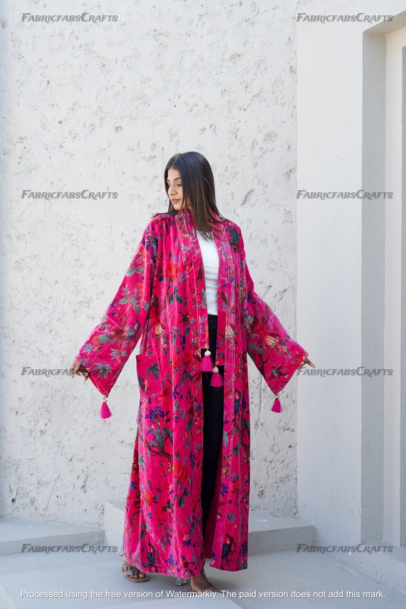 May include: A long, pink velvet robe with a floral print and tassels. The robe has a shawl collar and long sleeves.