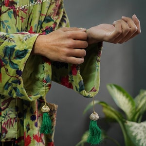 May include: A green velvet robe with a floral print and green tassel accents. The robe is being held by a person's hands.