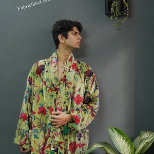 May include: A green velvet robe with a floral print featuring red, pink, and blue flowers and birds. The robe has a long sleeve and a sash tie.