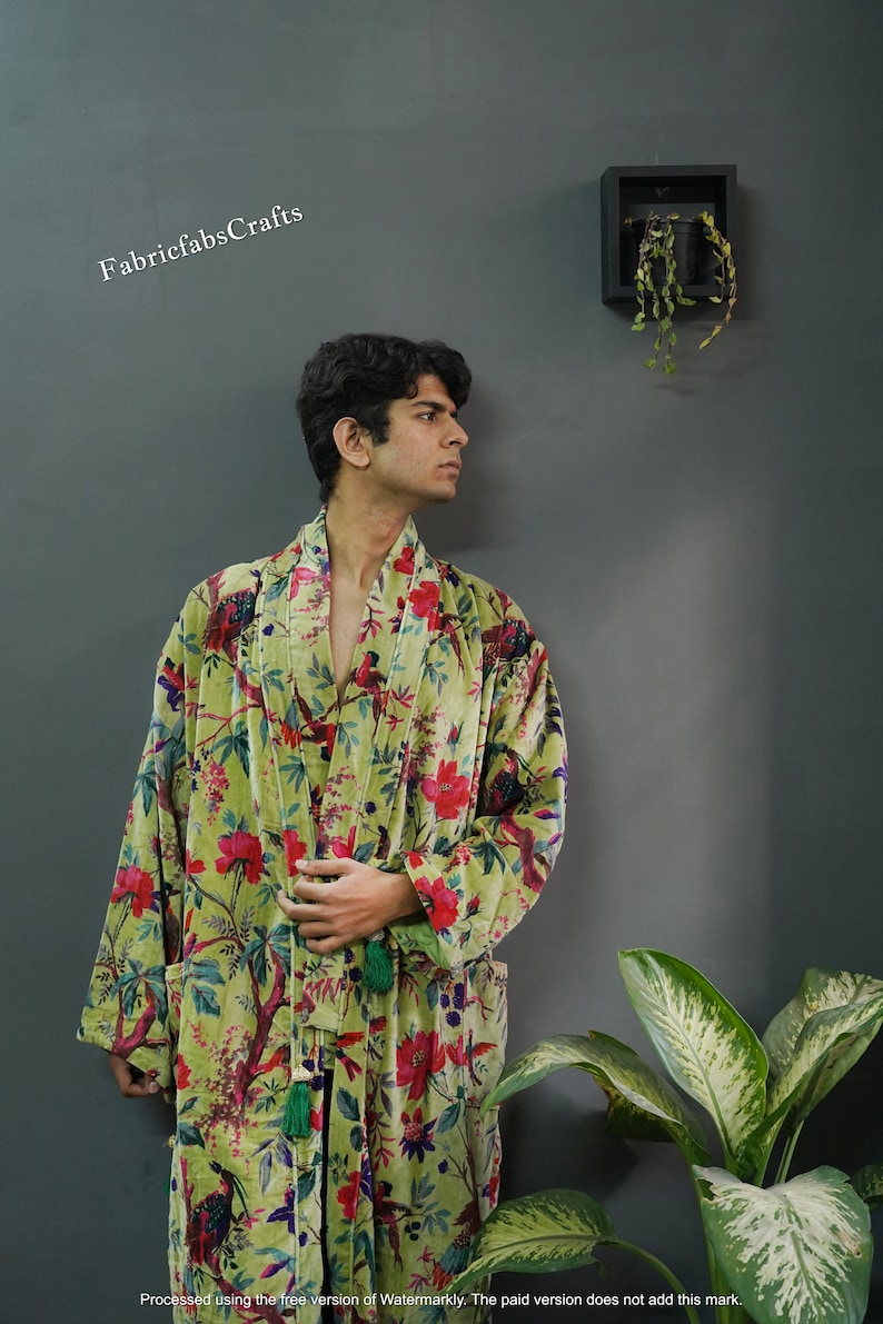 May include: A green velvet robe with a floral print featuring red, pink, and blue flowers and birds. The robe has a long sleeve and a sash tie.