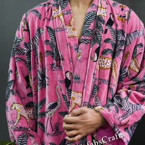 May include: Pink velvet robe with a jungle print featuring zebras, leopards, toucans, and palm trees. The robe has a tie closure and a pink tassel.