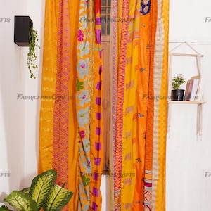 Puede incluir: Un conjunto de cortinas coloridas hechas de saris reciclados. Las cortinas son una mezcla de telas amarillas, naranjas, rosas y moradas con patrones florales y geom&eacute;tricos. Las cortinas est&aacute;n colgadas de una barra de cortina negra.