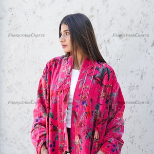 May include: A pink velvet kimono with a floral print and tassel details. The kimono has long sleeves and a relaxed fit.